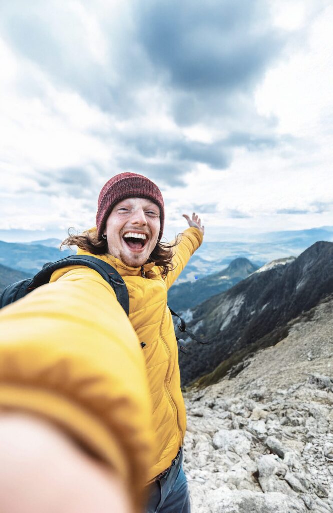 En person tar en selfie på toppen av et fjell. Personen smiler.