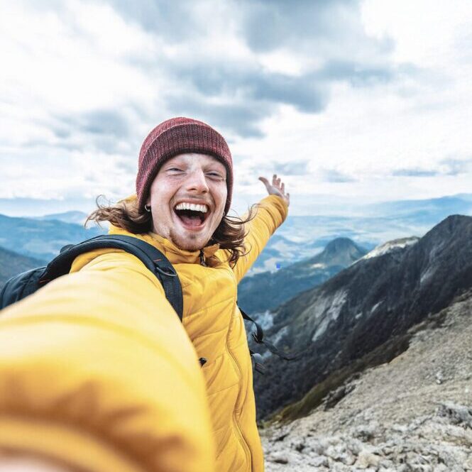 En person tar en selfie på toppen av et fjell. Personen smiler.